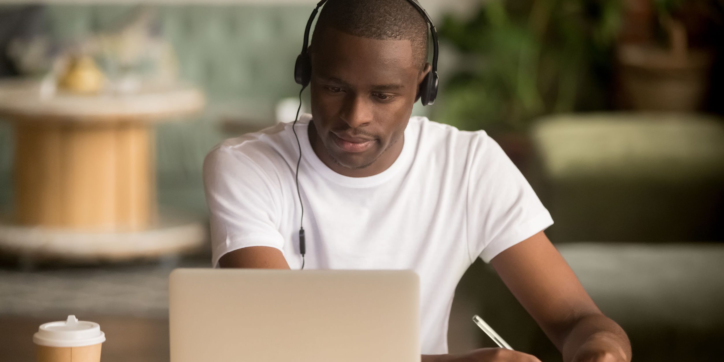 Focused african man wearing headphones watching webinar training making notes study online learning language on computer, black male student looking at laptop elearning in internet write information