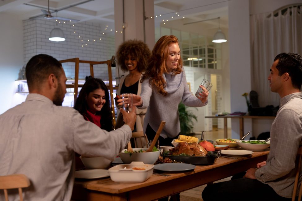 Front view of a group of five young adult multi-ethnic male and female friends sitting around a table and preparing to serve Thanksgiving dinner a home Employees' Thanksgiving